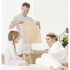 Mother Lies on a Bed Chatting to Her Young Daughter, Whilst Her Father Folds Towels in a Laundry Basket